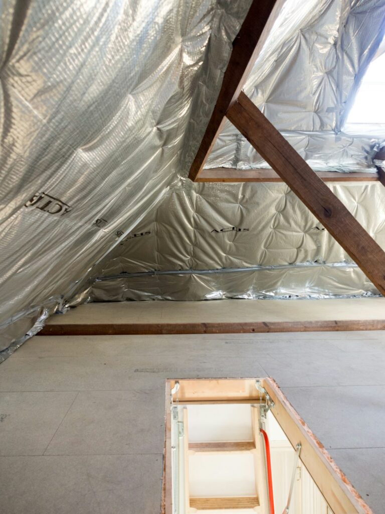Homeowner examining attic insulation beneath a residential roof with visible ventilation channels and roof framing.